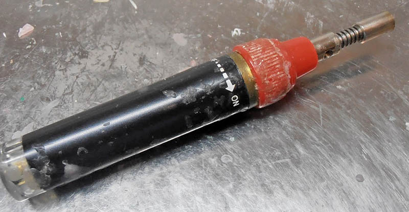 Petit chalumeau à gaz noir et rouge posé sur un plan de travail métallique