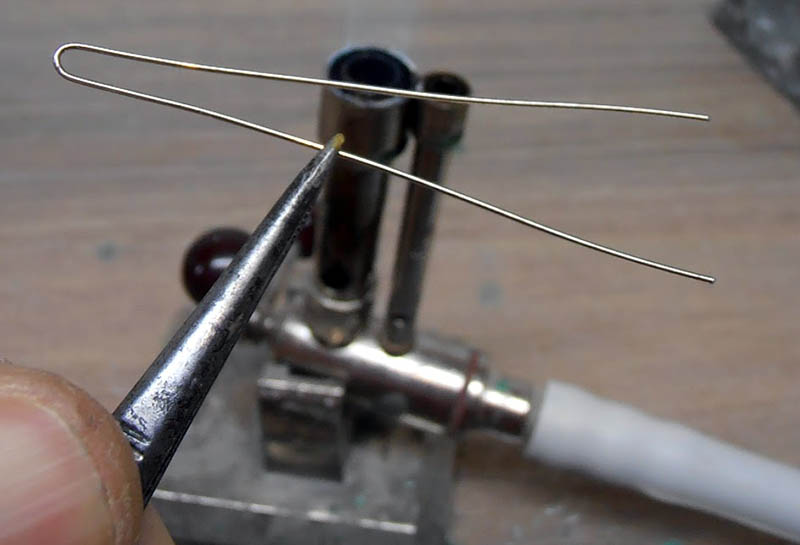 Soudure d'un fil de laiton plié maintenu par une pince, gros plan technique