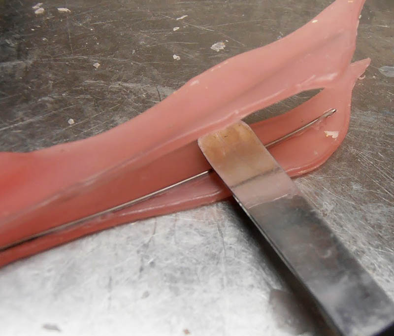 Gros plan sur une fine bande de pâte rose modelée à la spatule, armature métallique apparente