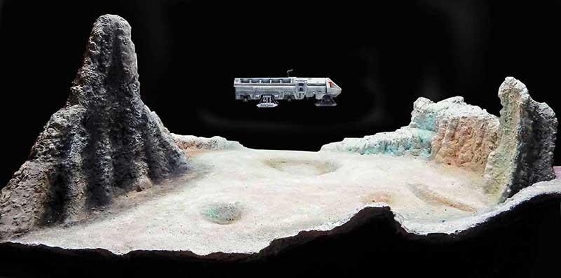 Maquette du Moonbus survolant un diorama de paysage lunaire avec cratères et reliefs rocheux