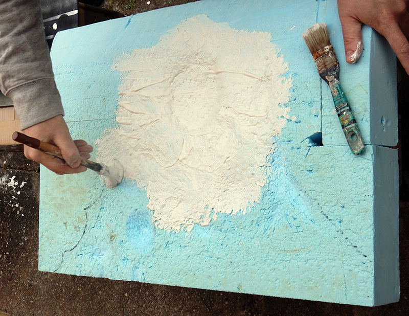 Application d'enduit blanc à la spatule sur un socle en mousse bleue avec pinceau