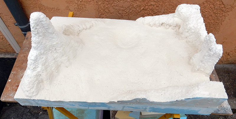 Diorama lunaire en plâtre blanc figurant un sol cratérisé avec reliefs rocheux, séchant en extérieur