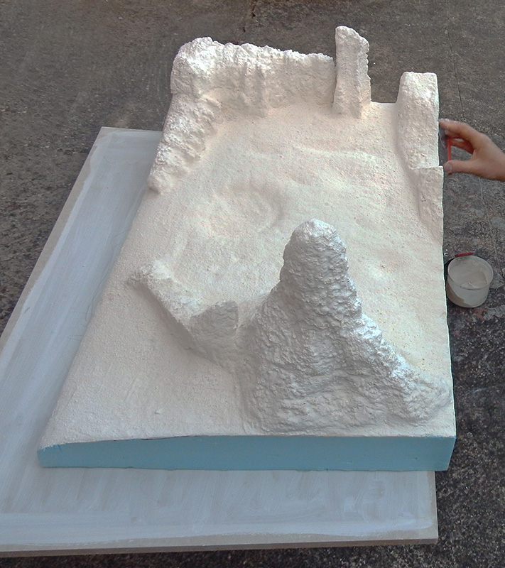 Diorama lunaire en plâtre blanc sur socle de mousse bleue en cours de modelage