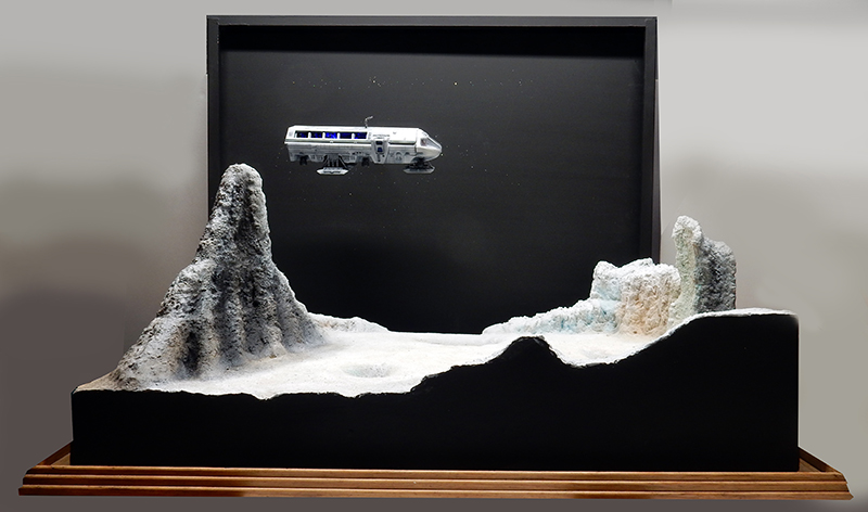 Maquette du Moonbus suspendu au-dessus d'un diorama lunaire avec montagnes rocheuses sur fond noir
