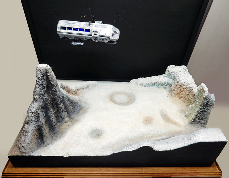 Maquette du Moonbus survolant un diorama de paysage lunaire avec cratères et reliefs montagneux