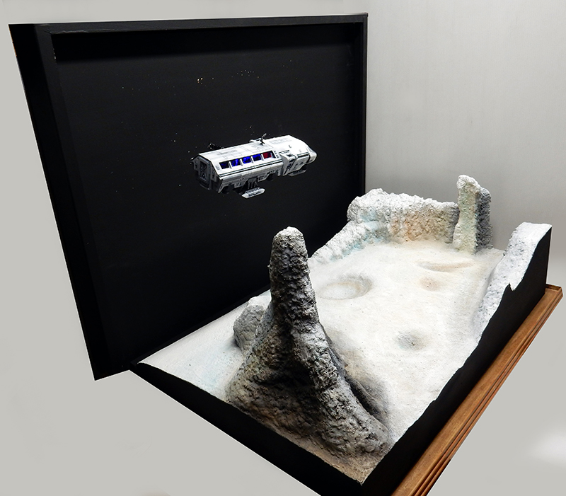 Maquette du Moonbus survolant un diorama lunaire avec cratères et reliefs rocheux escarpés