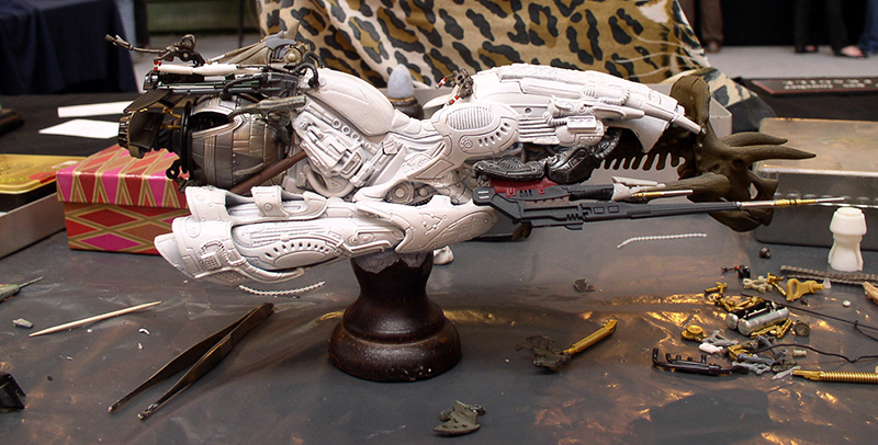 Maquette de motovolante blanche détaillée sur socle, entourée d'outils et pièces sur l'établi
