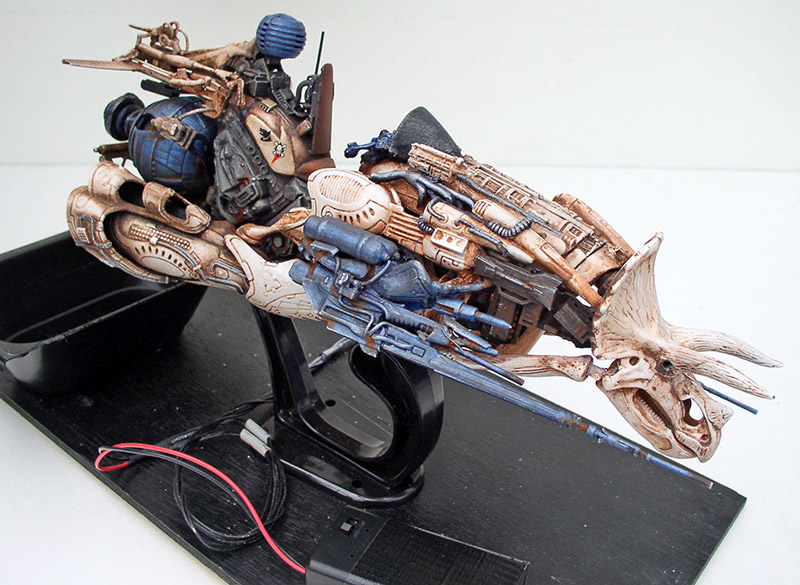 Maquette de motovolante steampunk au crâne de tricératops, pilote casqué bleu, sur socle noir