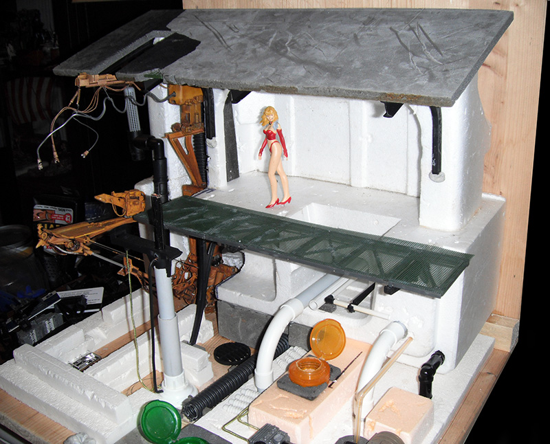 Maquette de diorama en cours de construction avec figurine féminine en rouge sur plateforme