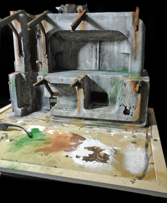 Maquette de bâtiment industriel en ruine peinte en gris, posée sur socle avec taches de peinture