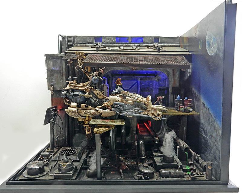 Diorama de maquette montrant une moto volante futuriste dans un atelier industriel délabré et sombre
