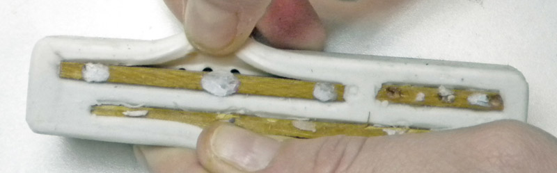 Moule souple en silicone blanc ouvert révélant des pièces en bois maintenu entre les doigts