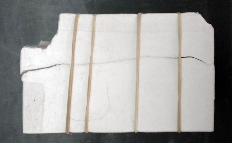 Coquille de plâtre blanche entourant le moule souple, maintenue fermée par des élastiques