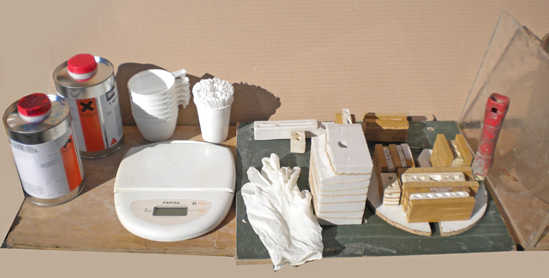 Matériel pour moulage silicone : bidons, balance, gobelets, gants et coffrages en bois sur établi