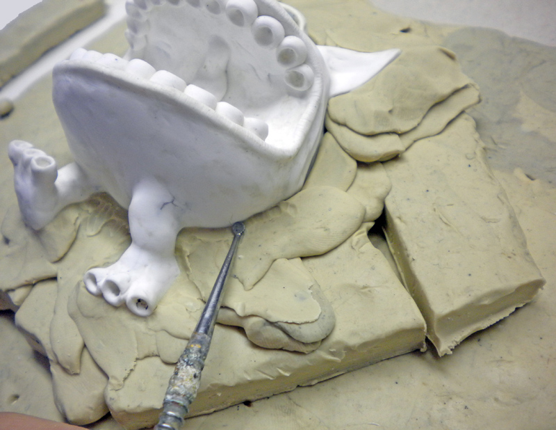 Modèle blanc en plâtre installé sur un lit de plastiline avec un outil de modelage