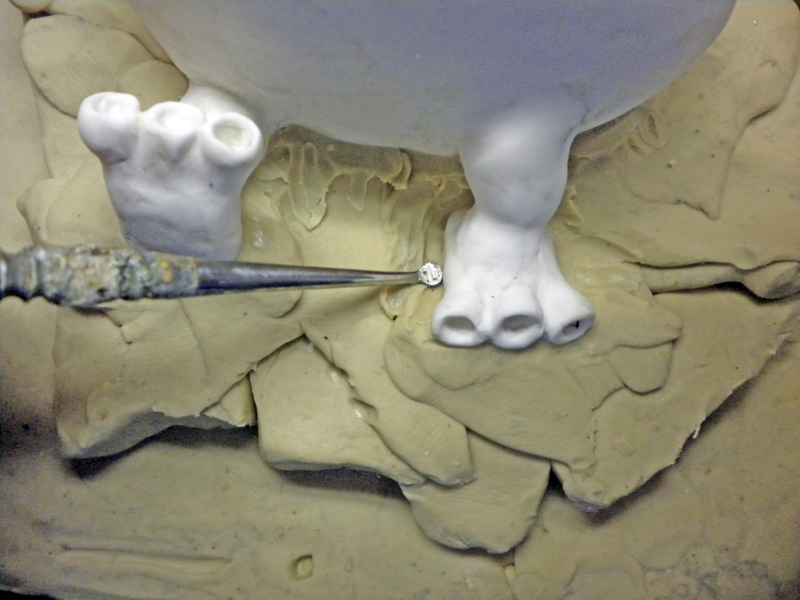 Modèle blanc enchâssé dans un lit de plastiline brune, pinceau appliquant l'élastomère sur les pattes