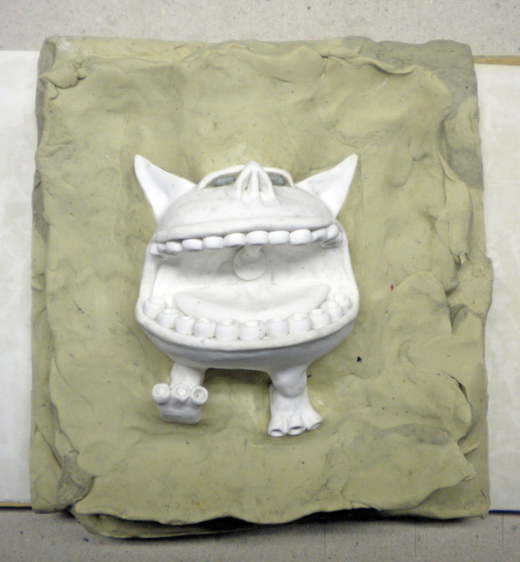 Figurine de monstre blanc à grande bouche enchâssée dans une plaque de pâte à modeler pour le moulage
