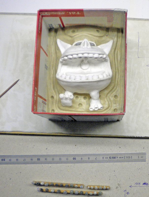 Figurine de créature blanche posée dans un moule silicone beige au sein d'une boîte en carton