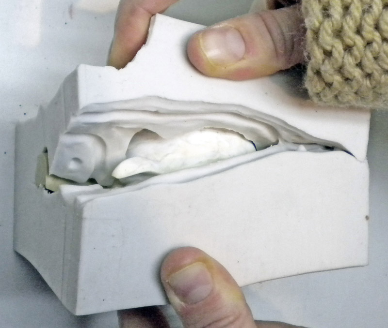 Mains ouvrant un moule en plâtre révélant l'empreinte en silicone blanc à l'intérieur