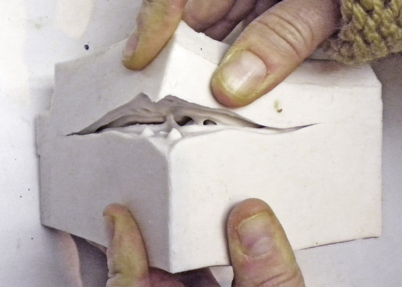 Mains ouvrant un moule en plâtre pour révéler l'empreinte souple en silicone à l'intérieur