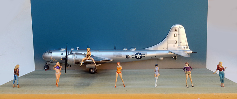 Maquette de bombardier B-29 argenté entouré de figurines féminines pin-up évoquant le thème nose art