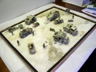 Diorama militaire avec véhicules et figurines miniatures peints sur un décor désertique encadré