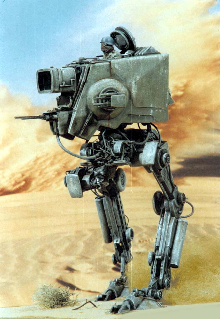 Maquette de robot marcheur bipède militaire avec pilote, photographiée devant un décor désertique