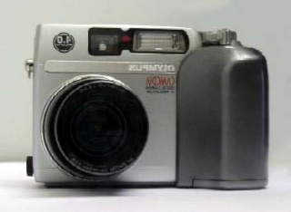 Appareil photo numérique compact Olympus argenté vu de face avec objectif et flash intégré