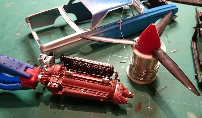 Maquette du moteur Allison peint en rouge et hélice rouge devant la carrosserie bleue de la Plymouth Belvedere