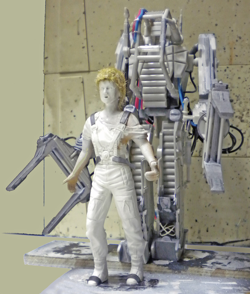 Maquette non peinte de Ripley devant l'exosquelette Powerloader gris en cours de montage