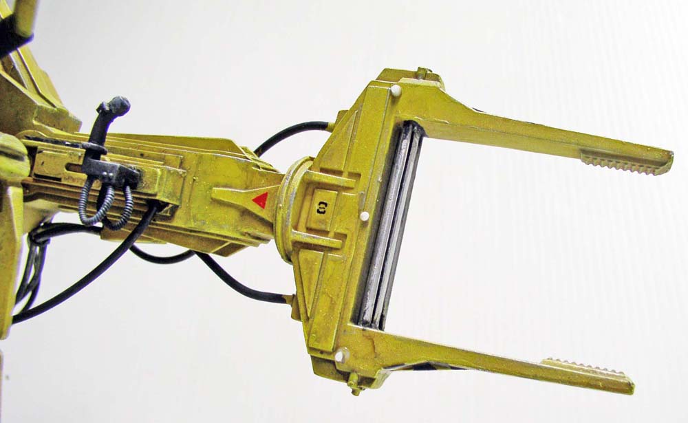 Bras manipulateur jaune du Powerloader avec pince mécanique ouverte et flexibles hydrauliques détaillés sur fond clair