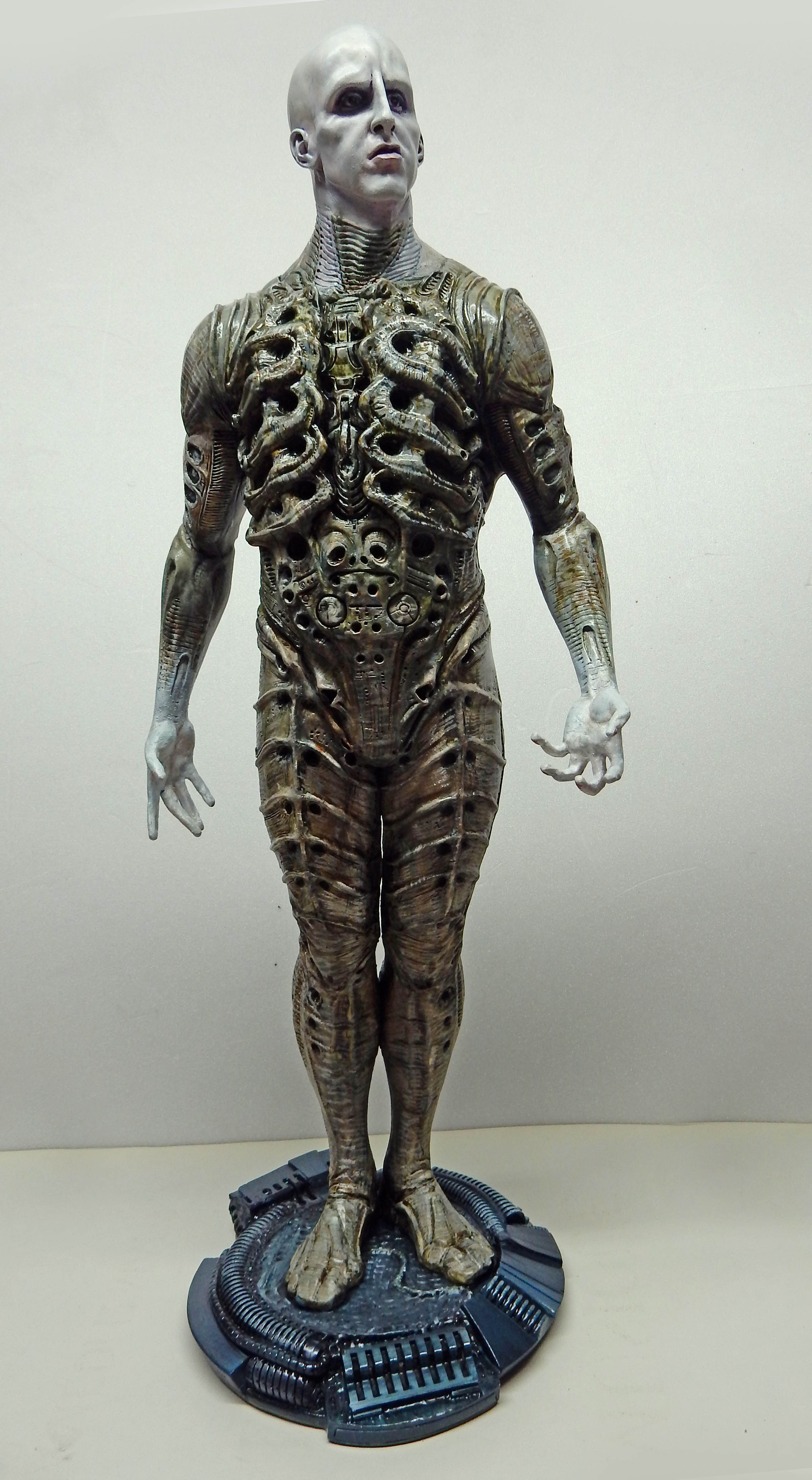 Figurine de l'Ingénieur Prometheus debout, corps musculeux biomécanique gravé, sur socle technologique