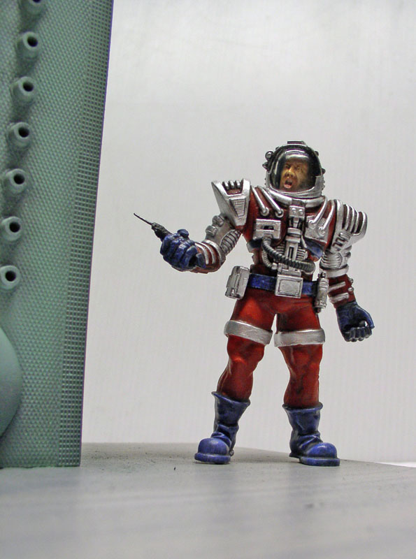 Figurine peinte d'astronaute en combinaison rouge et argent tenant un pistolet près d'une paroi