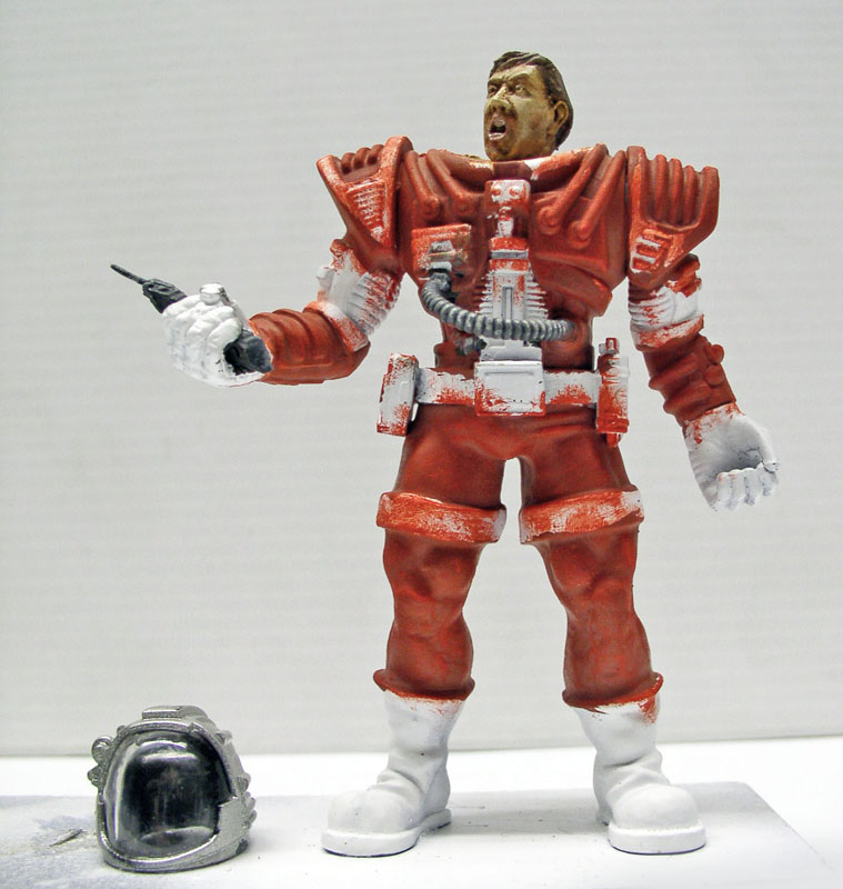 Figurine de pilote en combinaison spatiale rouge tenant un pistolet, casque posé au sol