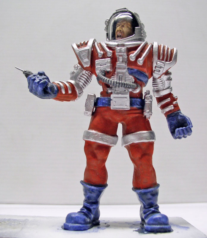 Figurine de héros spatial en combinaison rouge argentée et bottes bleues, casque transparent, brandissant un pistolet