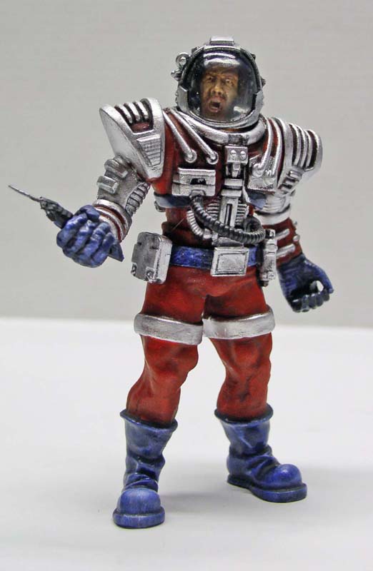 Figurine de spationaute en combinaison rouge et argentée avec bottes bleues tenant une arme