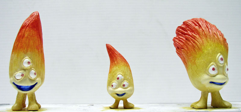 Trois figurines de créatures à flammes, trois yeux et cheveux orangés, peintes à différentes étapes