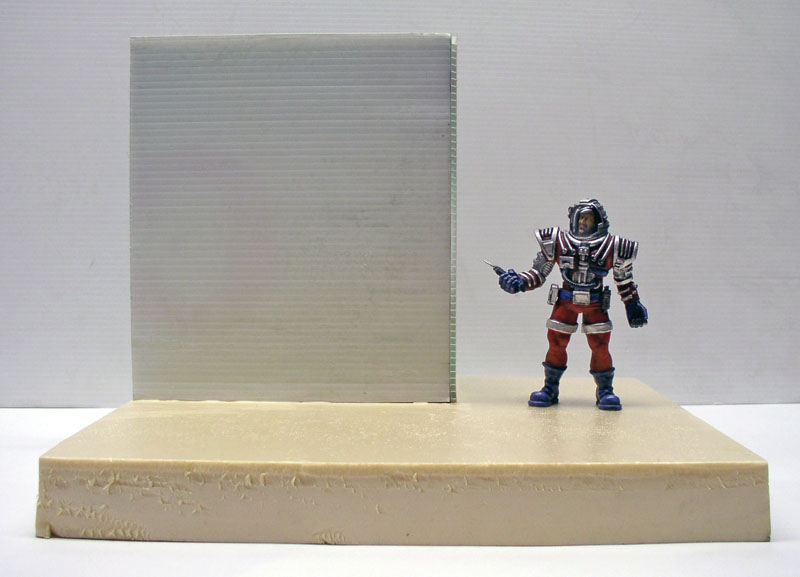 Figurine peinte d'astronaute en combinaison rouge et blanche près d'un mur translucide sur socle