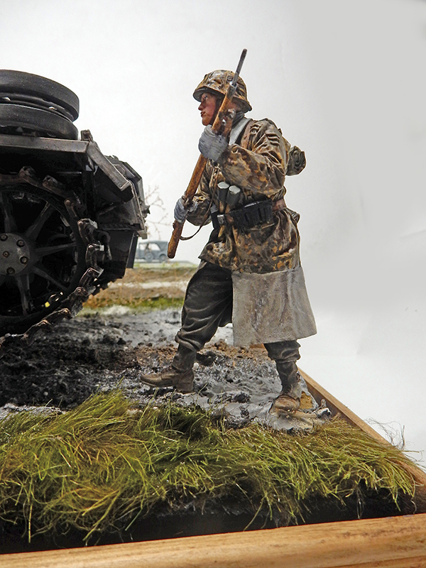 Figurine de soldat allemand en tenue camouflée marchant près du Panzer III sur diorama boueux