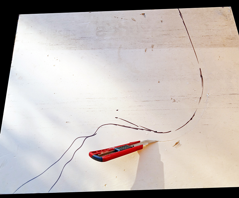Cutter rouge posé sur une plaque blanche avec tracé courbe dessiné au crayon