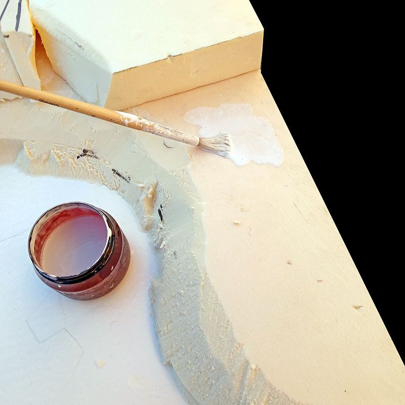 Application d'enduit gris sur maquette en mousse avec pinceau et pot près d'un décor