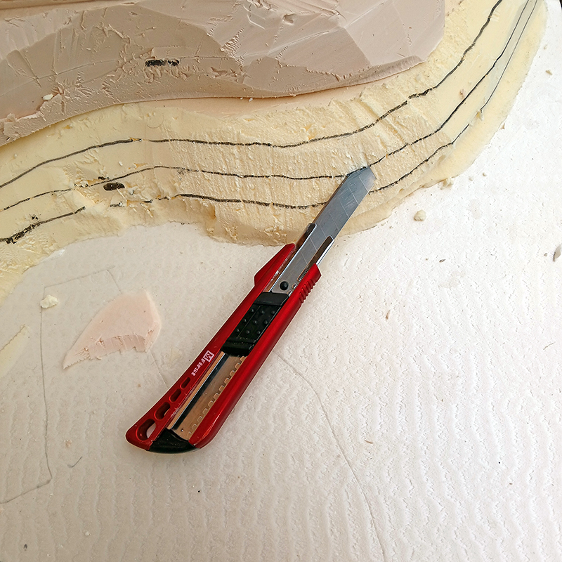 Cutter rouge posé sur un bloc de mousse découpé avec lignes de tracé pour la maquette