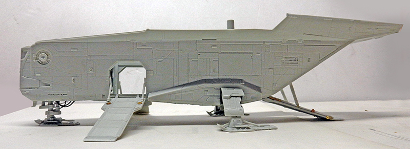 Maquette du vaisseau Razor Crest en apprêt gris vue de profil, rampe abaissée