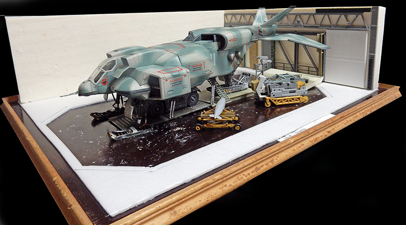 Maquette de vaisseau militaire dans un diorama de hangar avec engins au sol