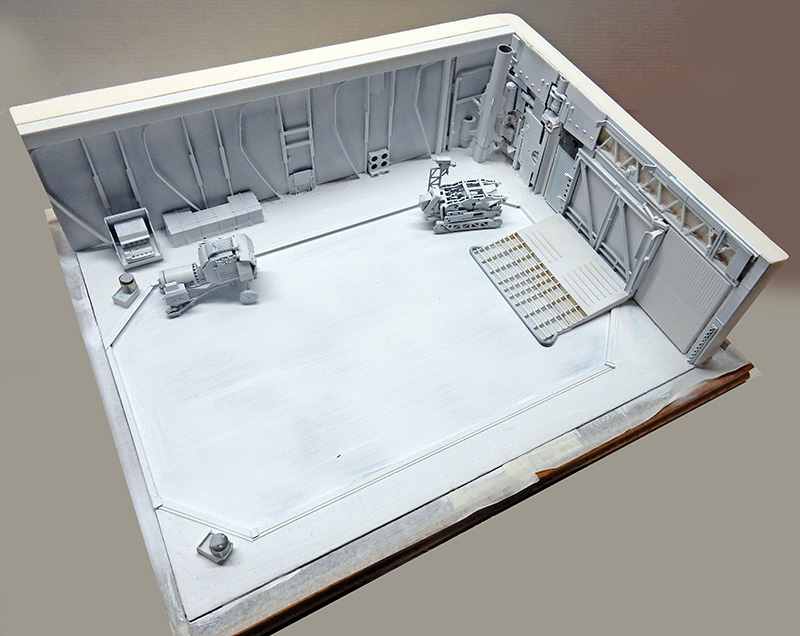 Maquette de décor de hangar spatial en gris et blanc avec véhicules et structures détaillées