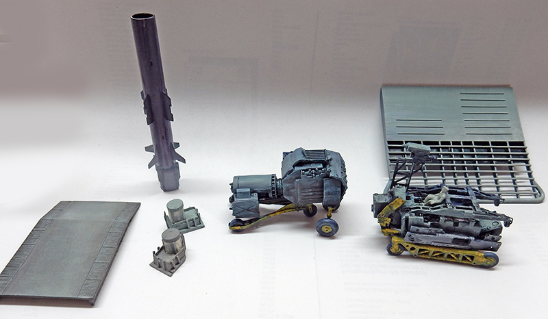 Éléments de décor militaire en maquette : missile, engins mécaniques et plateformes peints en gris