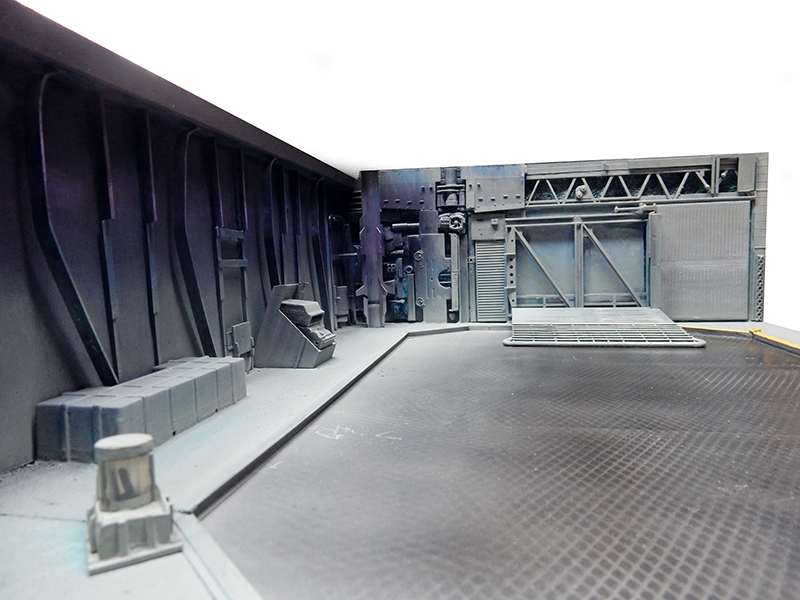Maquette de décor industriel science-fiction gris avec parois nervurées, passerelles métalliques et structures techniques détaillées