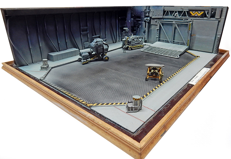 Diorama de hangar industriel science-fiction gris avec sol métallique, machines et cadre bois triangulaire