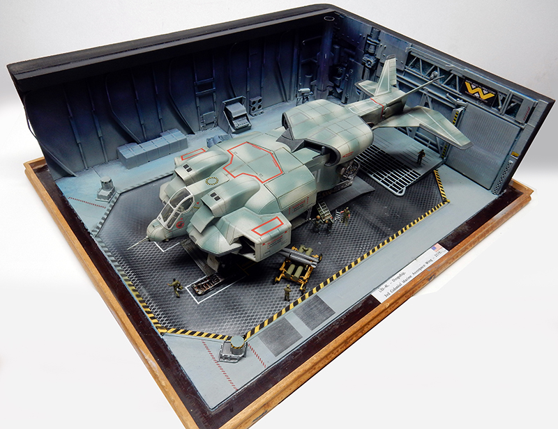 Maquette de vaisseau de combat futuriste dans un diorama de hangar militaire avec figurines