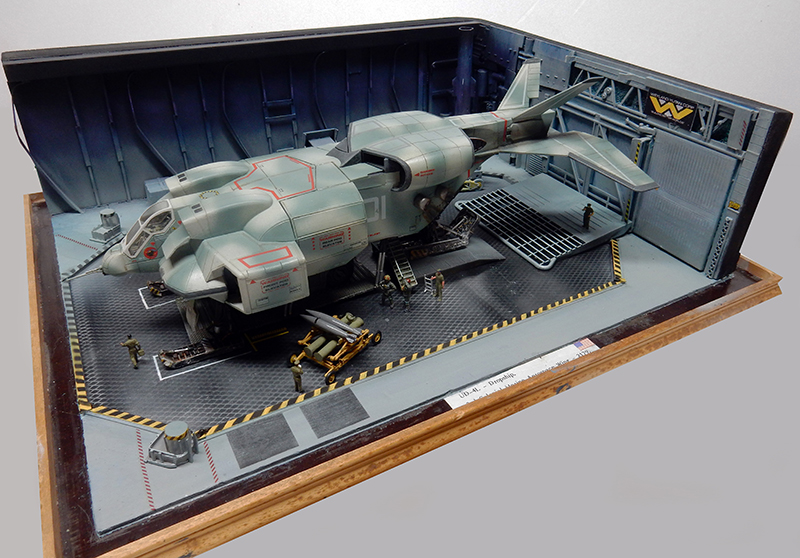 Maquette de vaisseau spatial militaire dans un hangar avec figurines et passerelle métallique